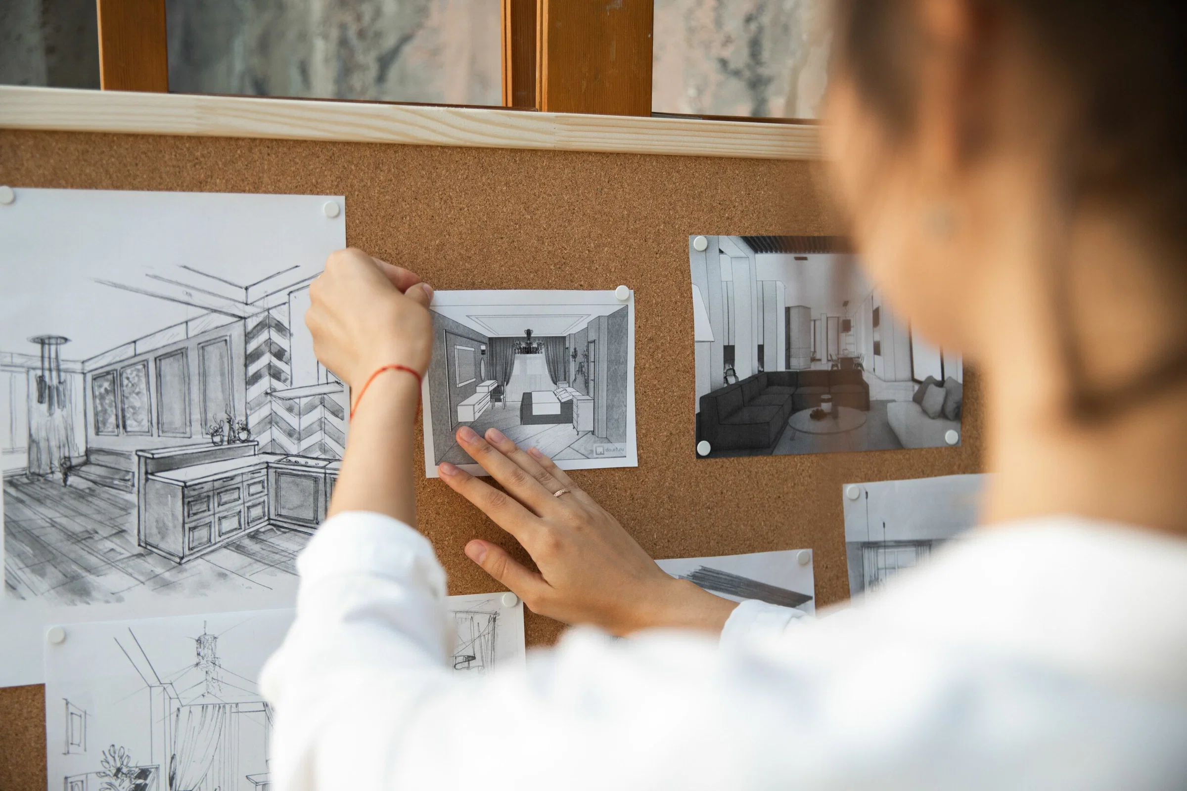Two people pinning black-and-white interior design sketches to a corkboard
