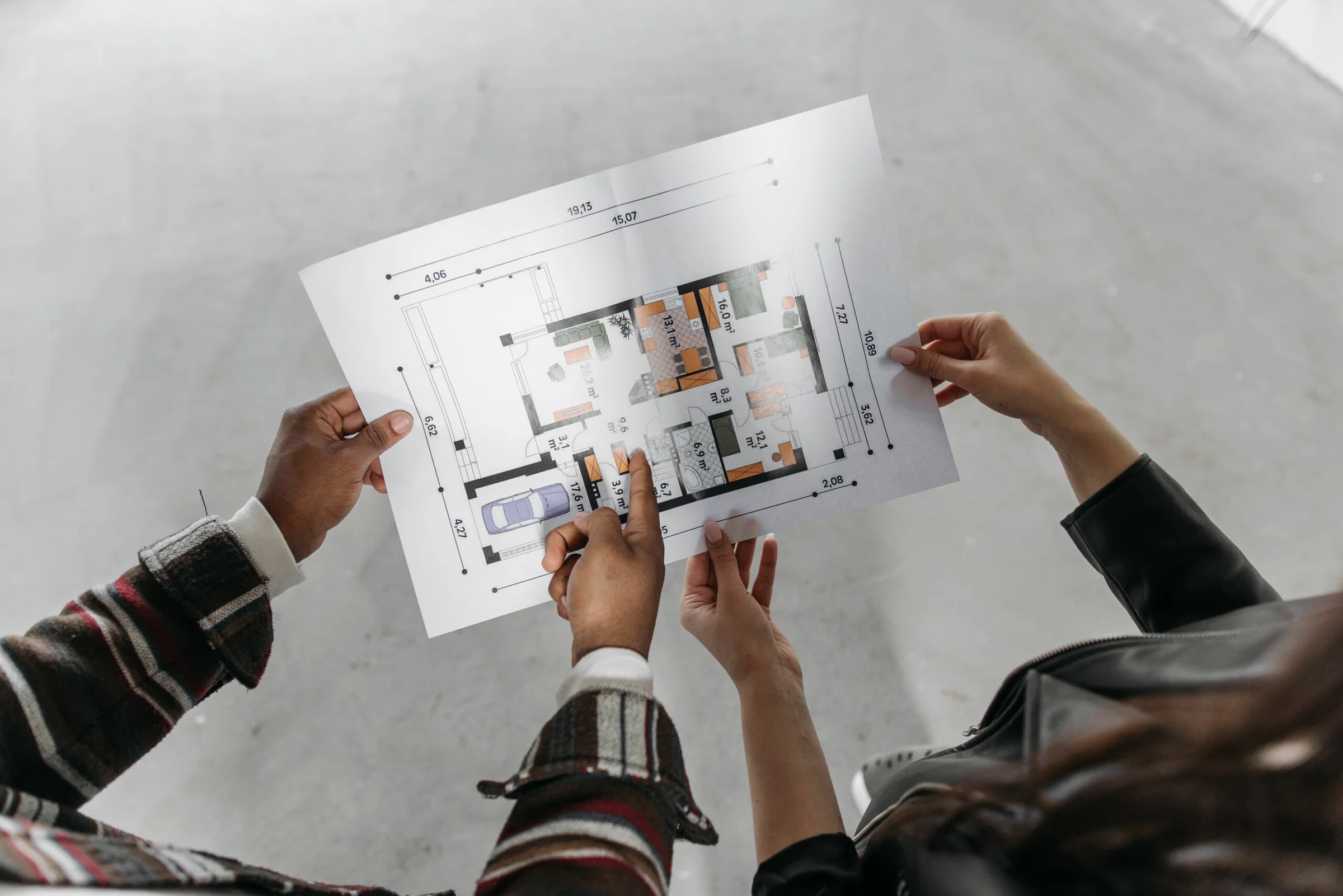 Two people hold and examine a detailed architectural floor plan outdoors, showing rooms and measurements.
