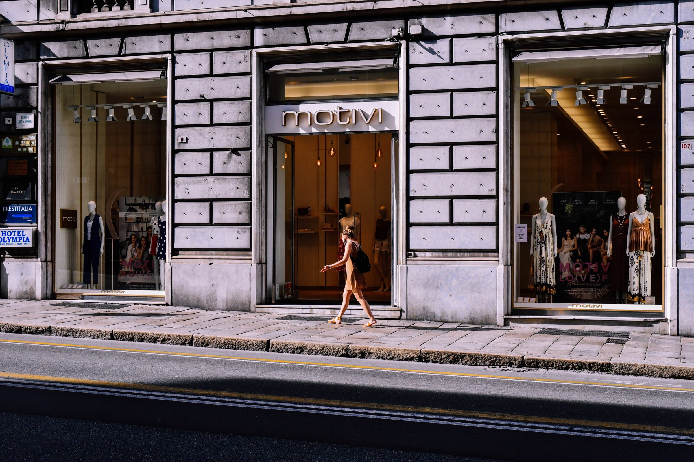 Motivi clothing storefront with mannequin window displays and a passerby walking by on a city street